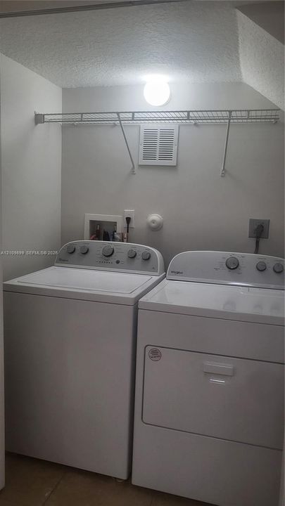 Laundry space featuring a white top-load washer and matching electric dryer with built-in overhead wire shelving