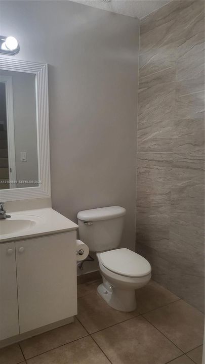 Vanity cabinet with integrated sink, framed wall-mounted mirror, ceramic tile flooring, and floor-to-ceiling textured tile accent wall