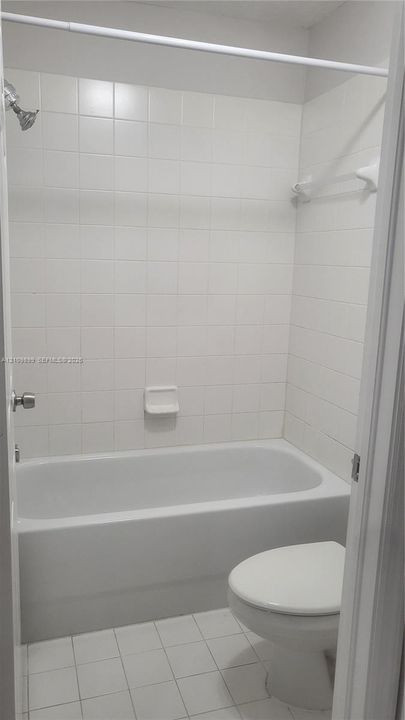 Full bathroom featuring a white porcelain tub with tiled surround, wall-mounted soap dish, and ceramic floor tile