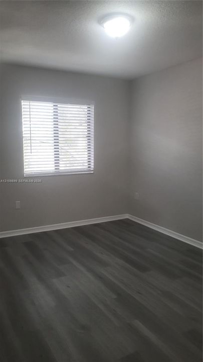 Neutral-toned walls, wood-finish flooring, horizontal blinds, and a flush-mount ceiling light fixture