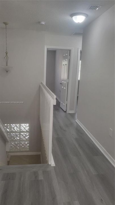 Hallway featuring wood-finish flooring, white railing with vertical balusters, glass block window detailing, and neutral wall tones