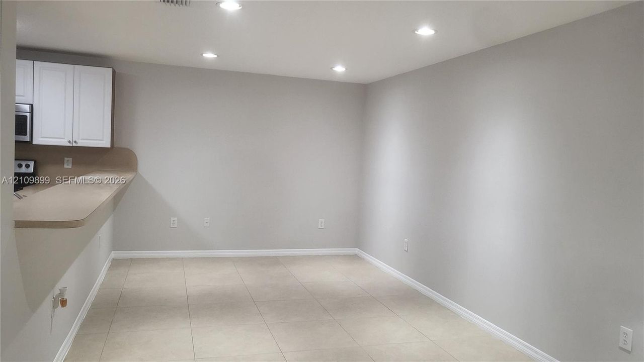 Neutral-toned tile flooring, recessed ceiling lighting, and a breakfast bar with a solid surface countertop