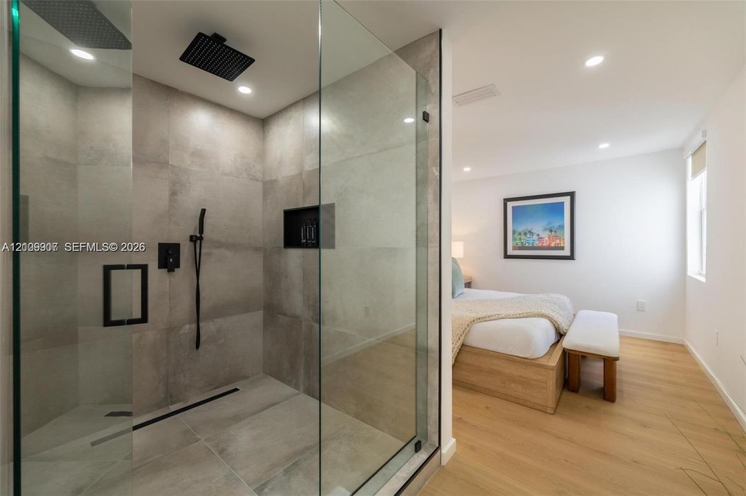 Walk-in shower featuring large-format stone-finish tile, glass enclosure, recessed wall niche, and matte black rainfall showerhead with handheld attachment