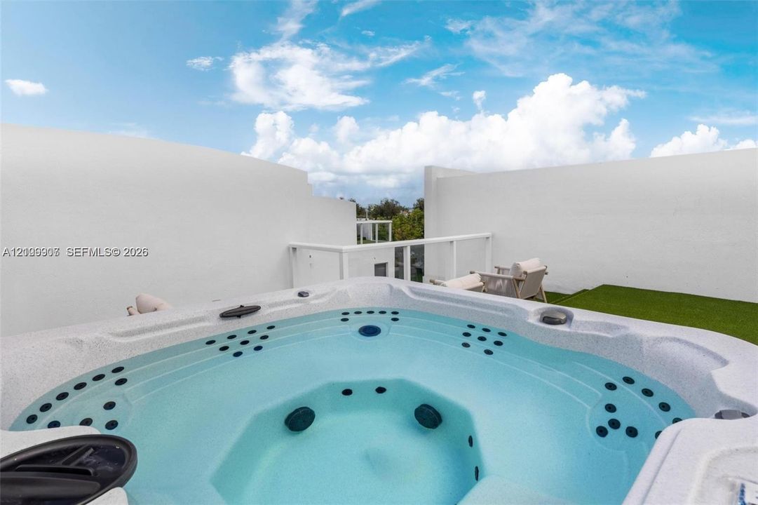 Rooftop terrace featuring a built-in spa, glass panel railing, and synthetic turf surfacing