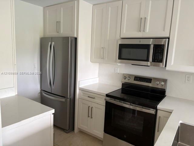Kitchen featuring white cabinetry with brushed metal hardware, solid-surface countertops, and a full suite of stainless steel appliances including a French-door refrigerator and built-in microwave