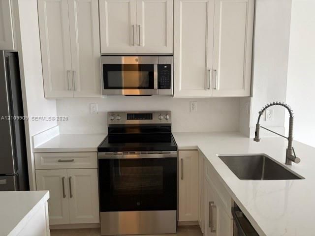 Kitchen featuring white shaker-style cabinetry, solid-surface countertops, stainless steel appliances, and a gooseneck faucet