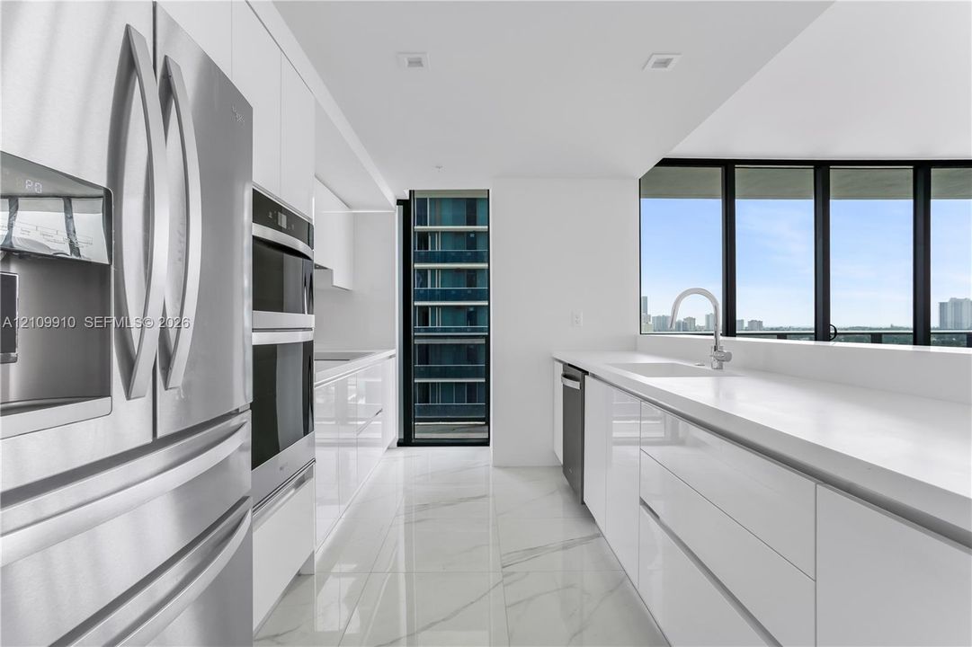 Contemporary kitchen featuring high-gloss cabinetry, stone-finish flooring, quartz countertops, stainless steel appliances, and floor-to-ceiling windows