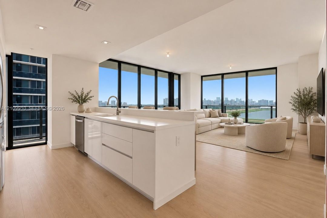 Kitchen featuring white flat-panel cabinetry, light-toned stone countertops, and stainless steel dishwasher, complemented by floor-to-ceiling windows and wood-finish flooring
