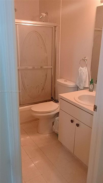 Bathroom featuring a tub-shower combination with an etched glass sliding door, vanity cabinet with integrated sink, tiled flooring, and wall-mounted mirror