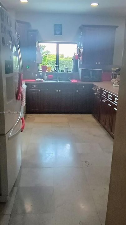 Kitchen featuring dark-finish cabinetry, neutral tile flooring, recessed ceiling lighting, and a double-basin sink positioned beneath a window