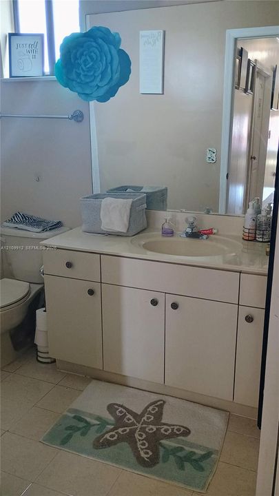 Vanity with integrated sink and countertop, full-width wall mirror, and neutral tile flooring