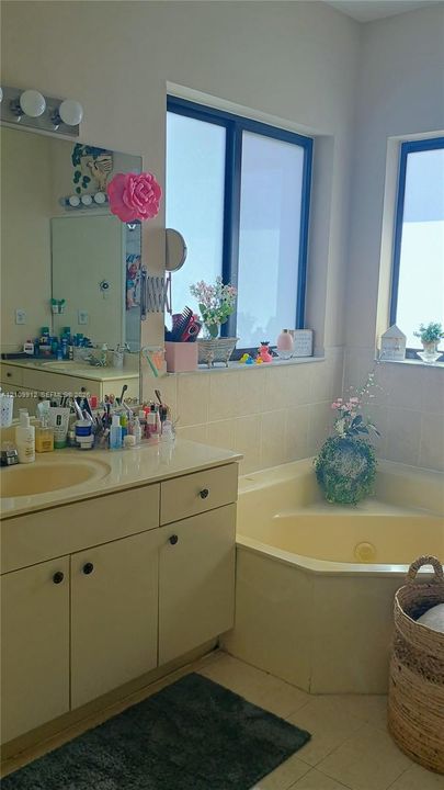 Bathroom featuring a corner soaking tub, solid-surface vanity countertop with integrated sink, wooden cabinetry, and dual windows