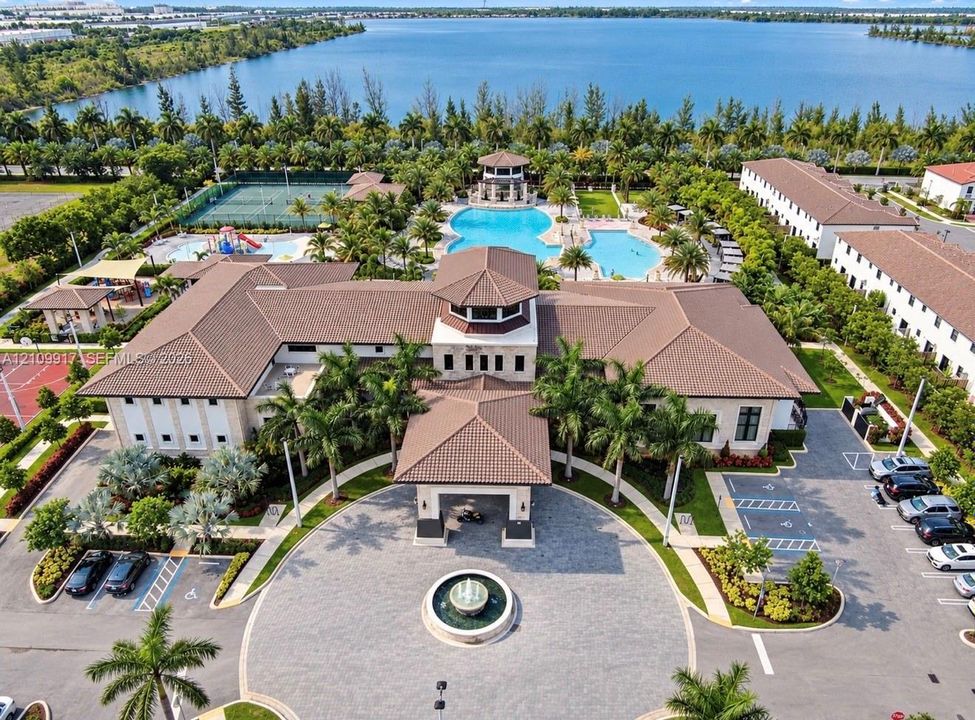 Community clubhouse featuring a porte-cochère, central fountain, swimming pool, tennis court, and water frontage
