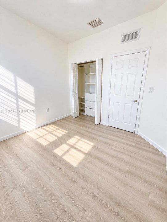 Room featuring wood-finish flooring, a six-panel interior door, and a built-in closet with integrated shelving and drawer storage