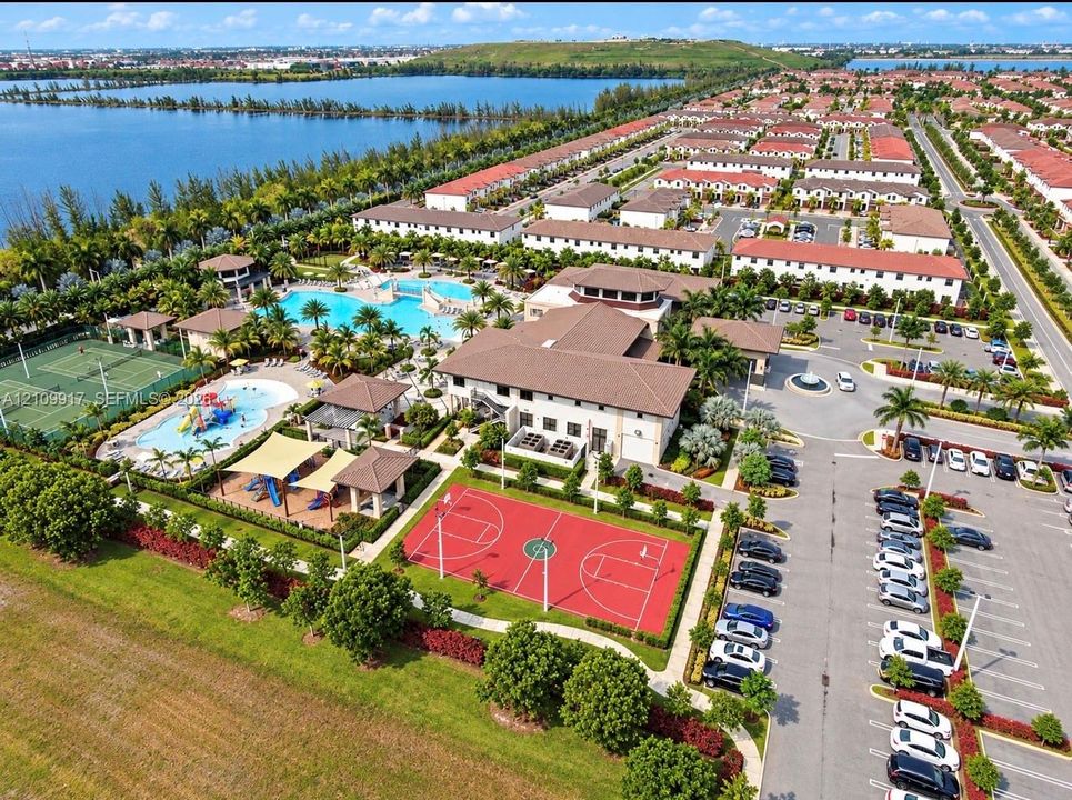 Aerial perspective featuring a swimming pool, multiple tennis courts, a basketball court, a splash pad, and waterfront grounds