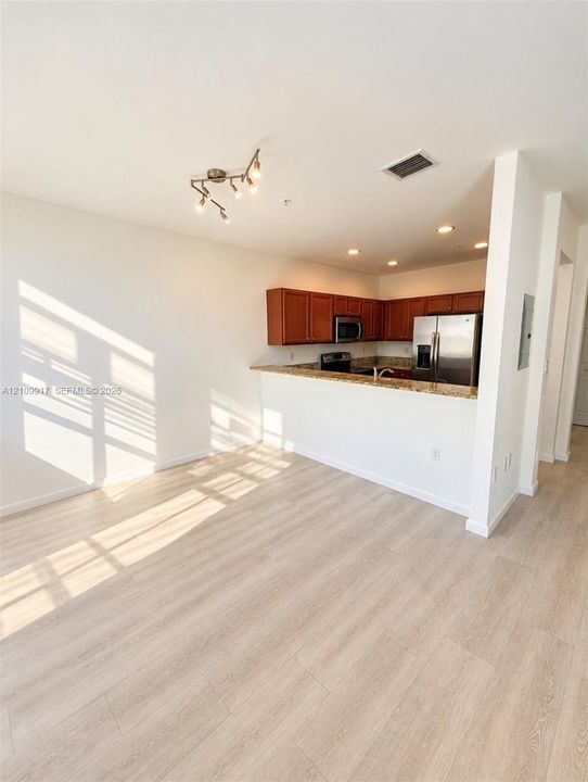 Kitchen featuring wood-finish cabinetry, stone countertops, stainless steel appliances, wood-finish flooring, and multi-directional overhead lighting