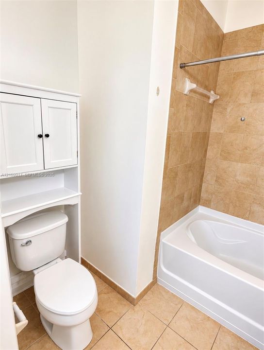 Bathroom featuring a white built-in storage cabinet, porcelain toilet, soaking tub, neutral-tone tile surround, and tile flooring