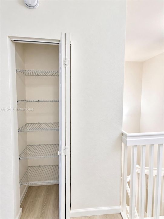 Storage closet featuring bi-fold doors, five tiers of wire shelving, and wood-finish flooring, accompanied by a white baluster railing
