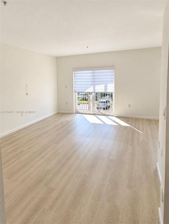 Open-concept living space featuring wood-finish flooring, neutral wall paint, and a sliding glass door providing access to a private balcony