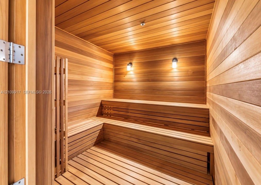 Sauna featuring wood paneling, multi-level built-in wooden benches, and wall-mounted lighting