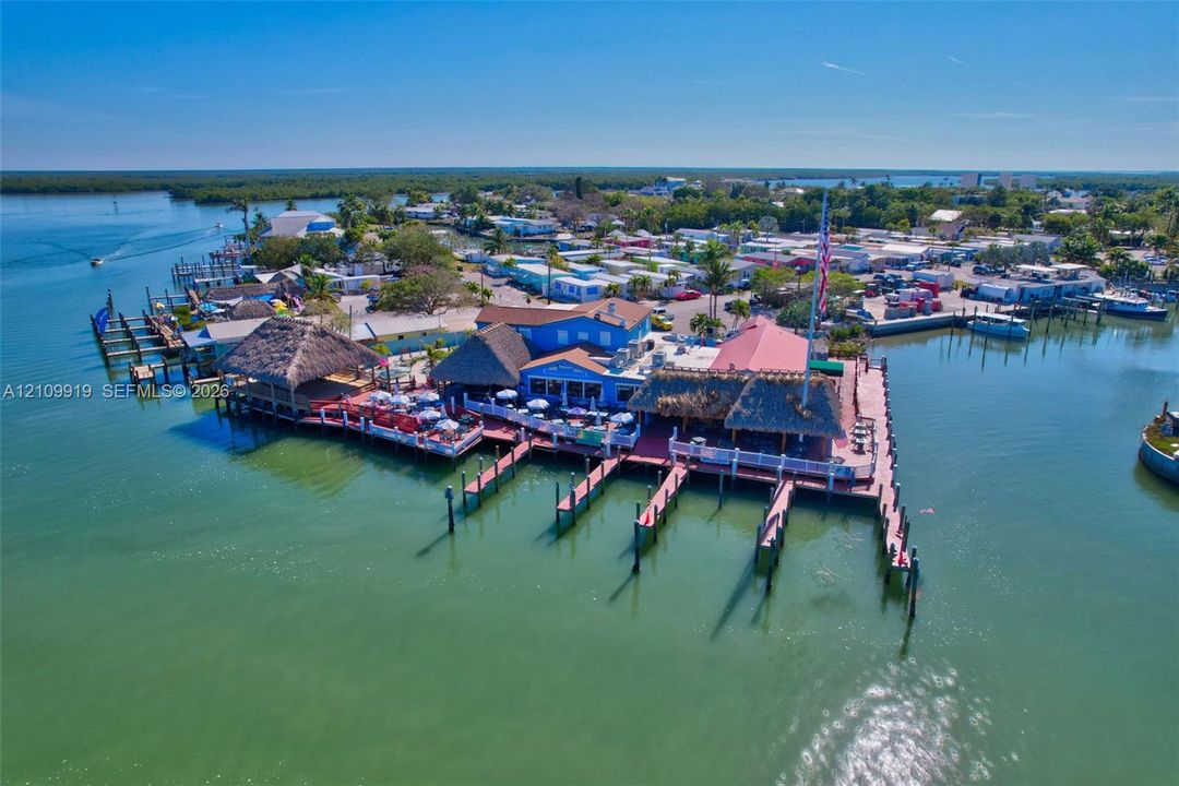 Waterfront property featuring multiple boat slips, thatch-roofed outdoor covered pavilions, and expansive wood-plank decking