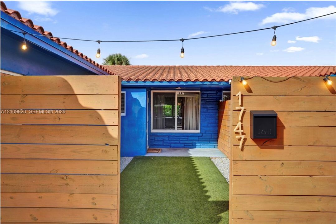 Residence 1747 (Left Side) – Private courtyard entrance featuring wood privacy fencing, and low-maintenance artificial turf and hurricane impact glass door.