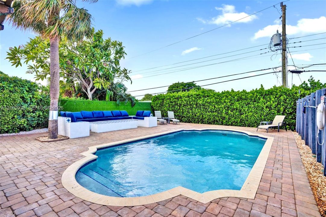 Residence 1747 (Left Side) – Private outdoor oasis featuring a heated swimming pool, built-in seating area, outdoor TV, and a pergola with a newly installed flat roof, all within a fully enclosed backyard designed for relaxation and entertaining.