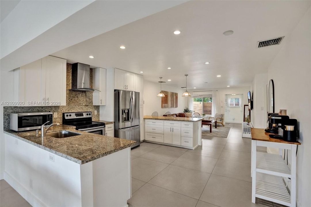 Kitchen featuring white shaker-style cabinetry, stone-surface countertops, stainless steel appliances, recessed lighting, and tile flooring
