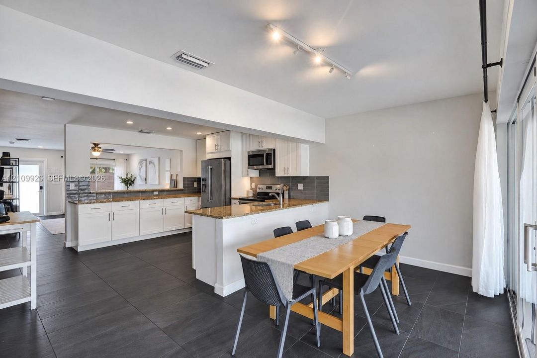 Residence 1747 (Left Side) – Kitchen featuring white cabinetry, granite countertops, stainless steel appliances, and a spacious dining area with hurricane-impact sliding glass doors overlooking the pool.