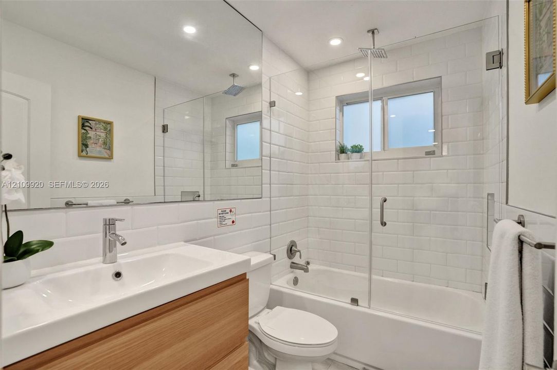 Residence 1747 (Left Side) Bathroom 2 featuring a wood-finish floating vanity with an integrated sink, polished chrome faucet, frameless glass-enclosed shower and tub combination, and floor-to-ceiling white subway tile