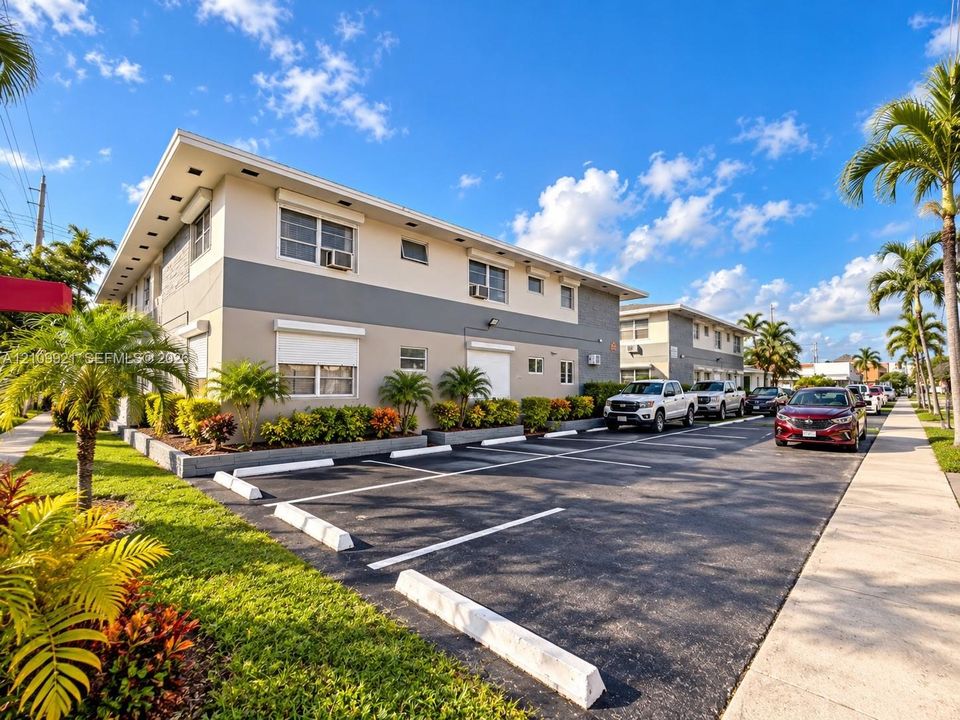 Multi-unit exterior featuring two-story modern architecture, exterior neutral-toned stucco siding, dedicated asphalt parking area, and landscaped grounds with mature palm trees