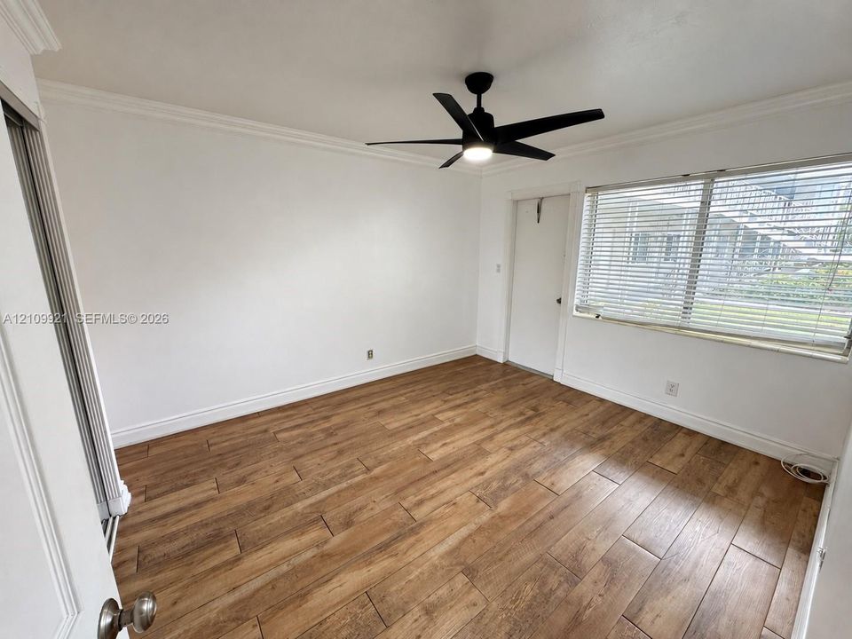 Wood-finish tile flooring, neutral walls, crown molding, multi-blade ceiling fan with integrated light, and horizontal window blinds