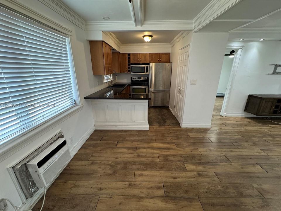 Kitchen featuring wood-finish flooring, dark stone countertops, wood cabinetry, stainless steel appliances, and ceiling crown molding