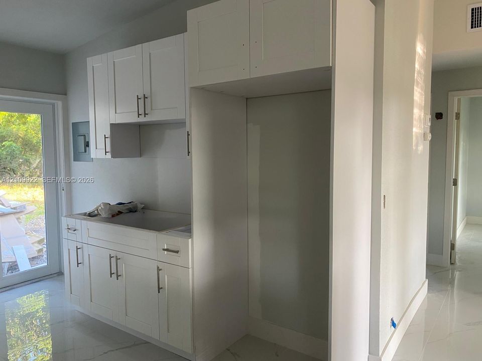 White cabinetry with matte metal hardware, stone-finish flooring, and a dedicated appliance enclosure
