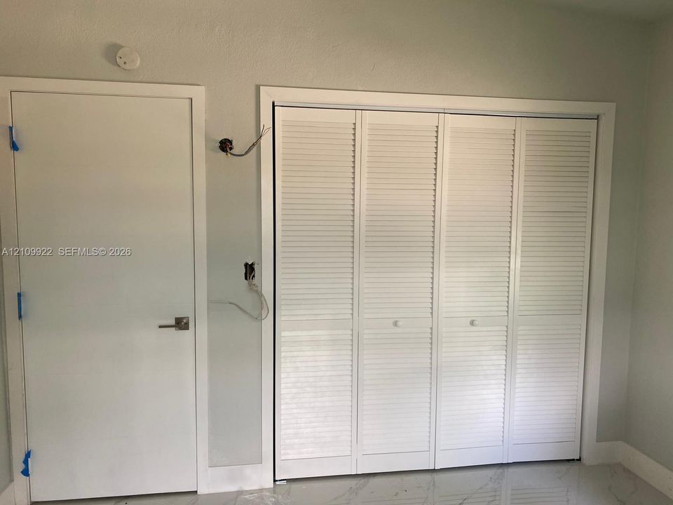 White louvered bifold closet doors and a coordinating solid-core interior door with a brushed nickel lever handle