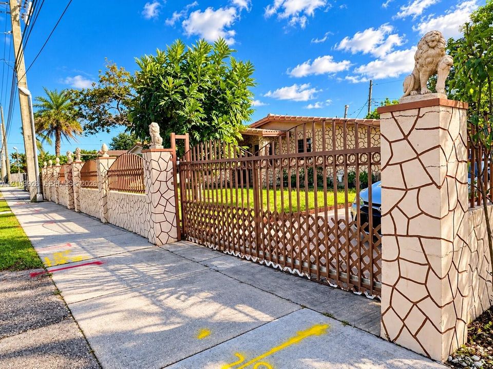 Fenced perimeter featuring stone-clad masonry pillars topped with decorative stone lion accents, complemented by a tall metal lattice gate