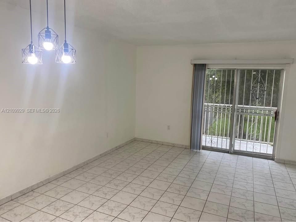 Interior space featuring tile flooring, a geometric three-light pendant fixture, and sliding glass doors with integrated metal security bars