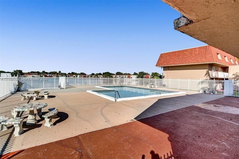 Swimming pool with a metal perimeter fence, concrete decking, and stationary stone-composite outdoor seating