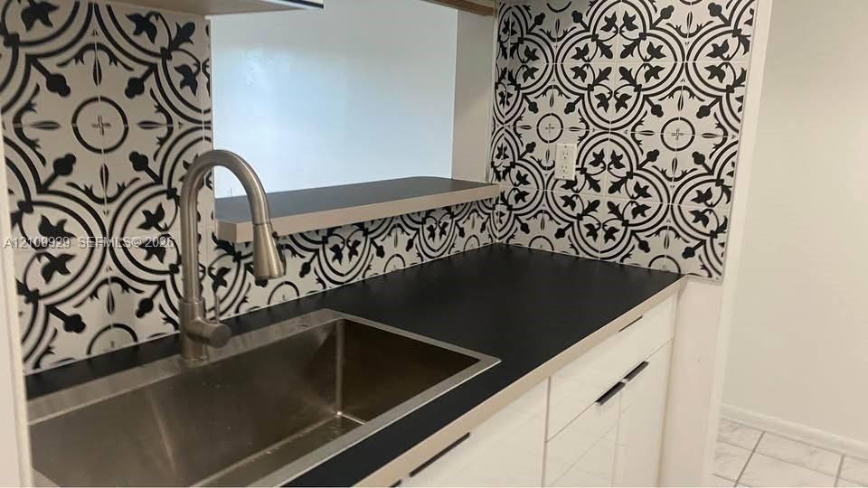 Kitchen featuring patterned tile backsplash, stainless steel undermount sink, high-arc pulldown faucet, solid surface countertop, and contemporary flat-panel cabinetry