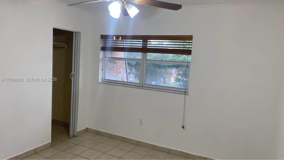 Room featuring ceramic tile flooring, a multi-blade ceiling fan with light kit, a sliding closet door, and a horizontal window with wooden blinds