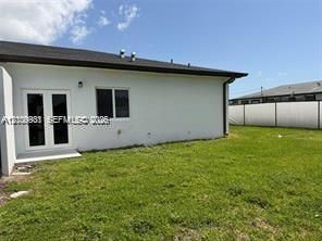 Exterior featuring a white stucco facade, dual-pane casement windows, French doors, and a solid perimeter privacy fence enclosing the rear lawn
