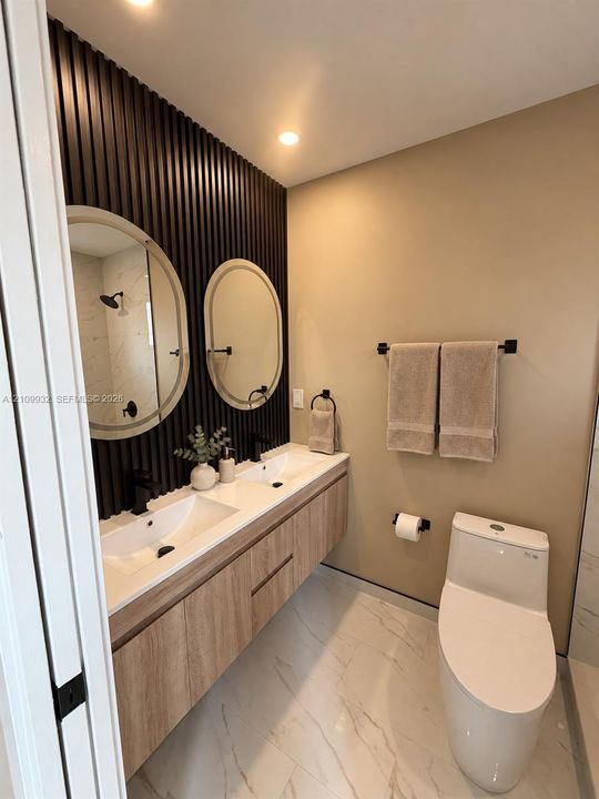 Floating vanity with wood-finish cabinetry, dual vessel sinks, matte black fixtures, textured slat accent wall, and porcelain tile flooring