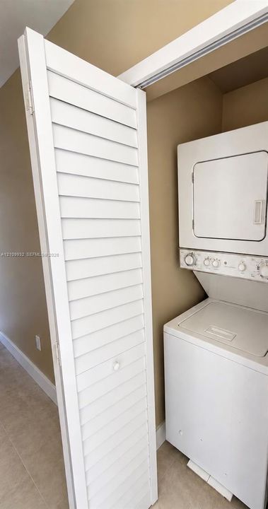 Laundry closet featuring a space-saving stacked washer and dryer unit concealed by white louvered bifold doors