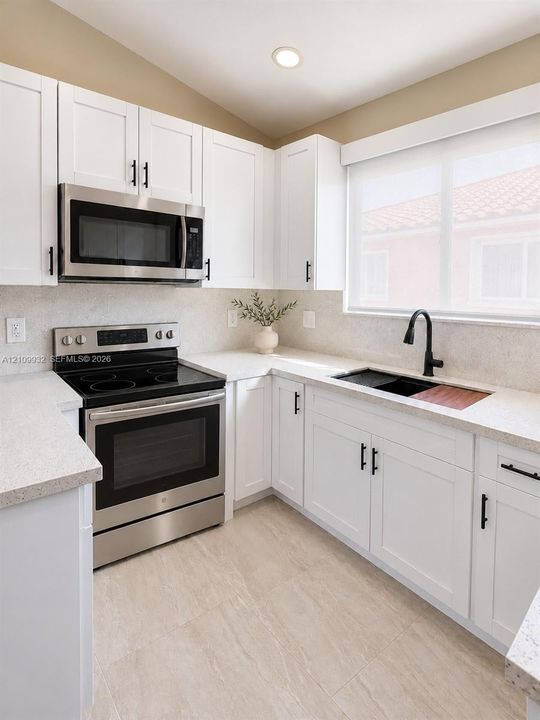 Kitchen featuring white Shaker-style cabinetry, stainless steel appliances, speckled stone-finish countertops, matte black hardware, and a drop-in sink with a high-arc faucet