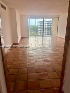 Living area featuring earth-toned ceramic tile flooring, floor-to-ceiling glass sliding doors, and a metal-railed balcony