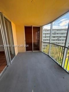 Covered balcony featuring concrete flooring, sliding glass door access, and a metal railing enclosure