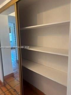 Storage closet featuring floor-to-ceiling mirrored sliding doors and multi-tier white built-in shelving