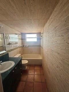 Bathroom featuring textured wall and ceiling treatments, terracotta tile flooring, a dark vanity cabinet with an integrated sink, and a porcelain soaking tub