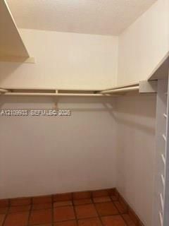 Storage area featuring built-in shelving, hanging rods, and tile flooring