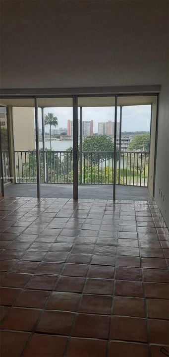 Terracotta tile flooring and floor-to-ceiling sliding glass doors opening to a screened-in balcony with water and skyline scenery